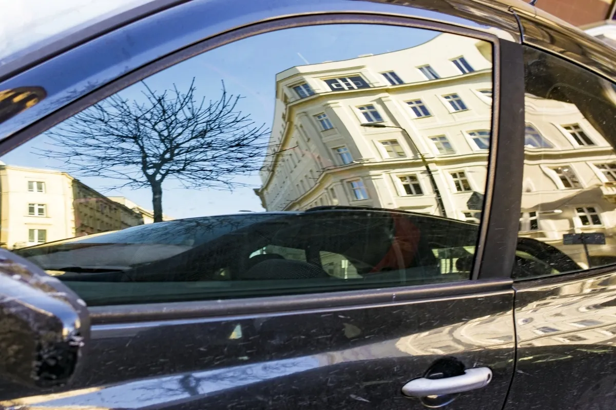 Street and cream-colored building reflected in a parked car door
